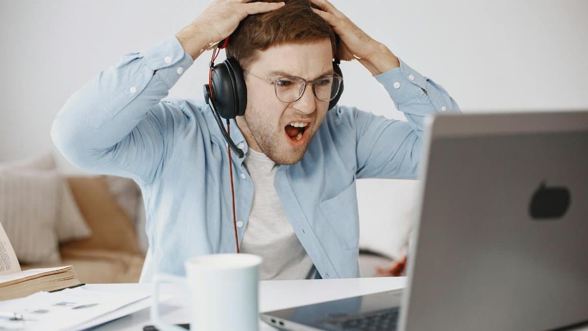 Man experiencing frustration at home office while working on laptop.