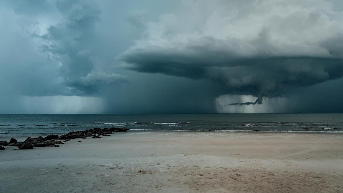 A powerful storm approaches a serene sandy beach with dramatic clouds and turbulent waves.