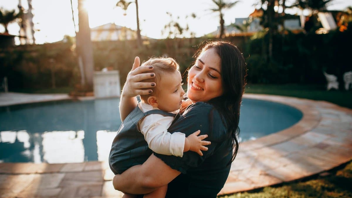 Joyful mother holding her young child by the pool during a sunset, capturing a serene moment.