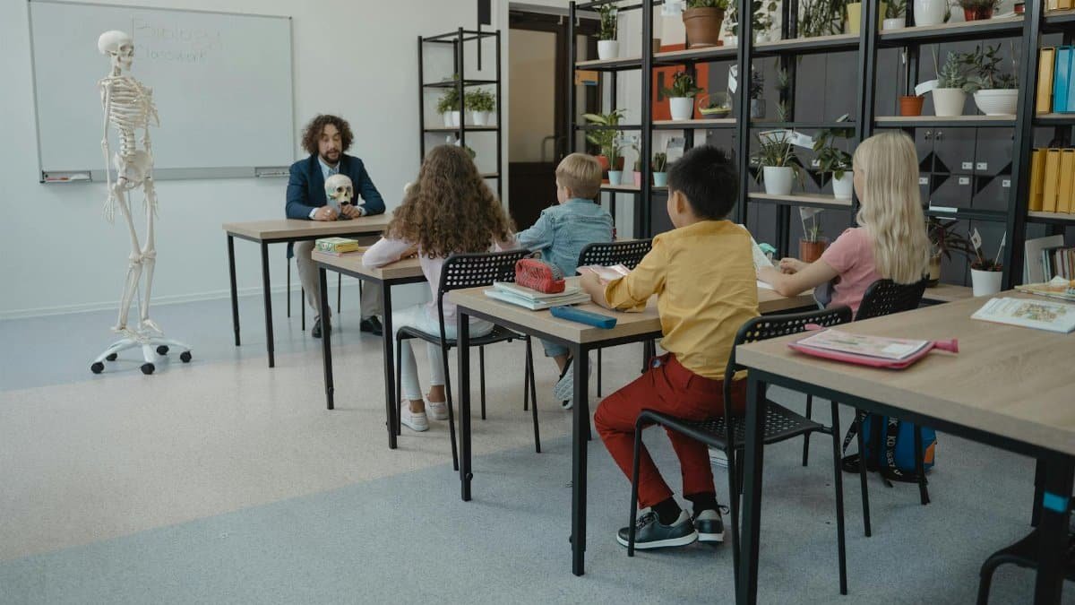 Children in an elementary classroom learning biology with a teacher and skeleton model.