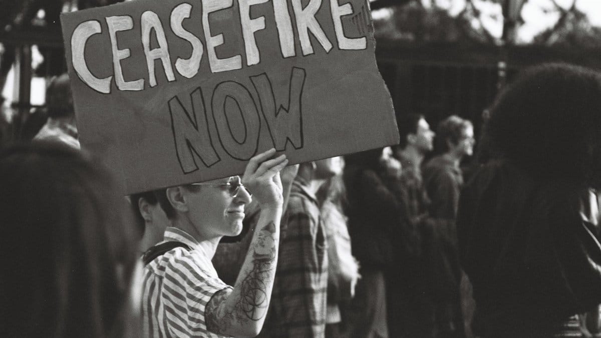 Black and white photo of a protest in Lisbon with a person holding a 'Ceasefire Now' sign.