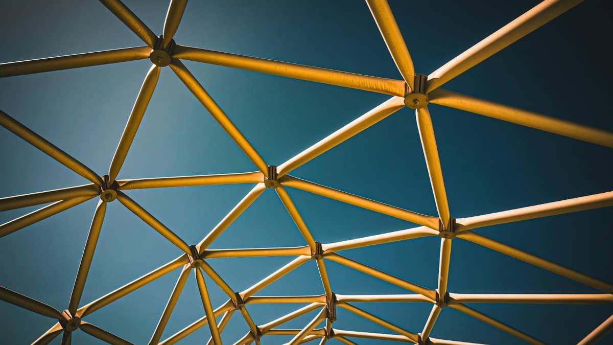 Dynamic geometric metal structure with triangular patterns against a blue sky, showcasing modern architectural design.