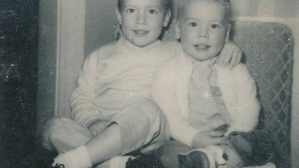 Charming vintage black and white photo of two young brothers sitting on a chair, smiling warmly.