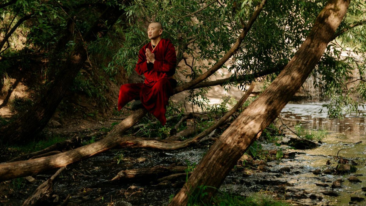 A serene monk in red robes meditates by a forest stream, embracing nature's tranquility.
