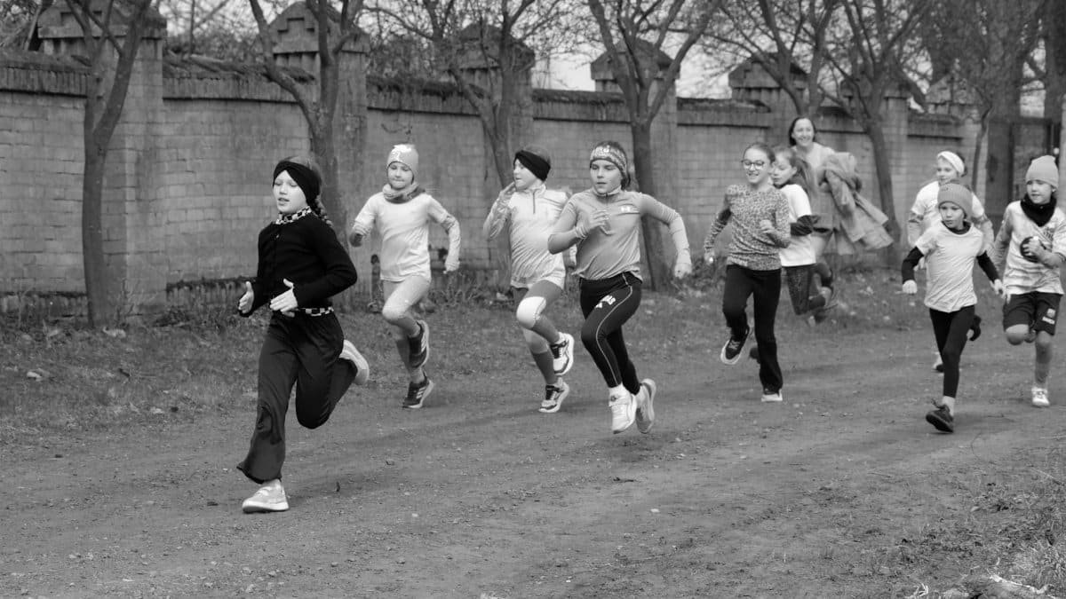 A group of children enthusiastically running on an outdoor pathway during the day.