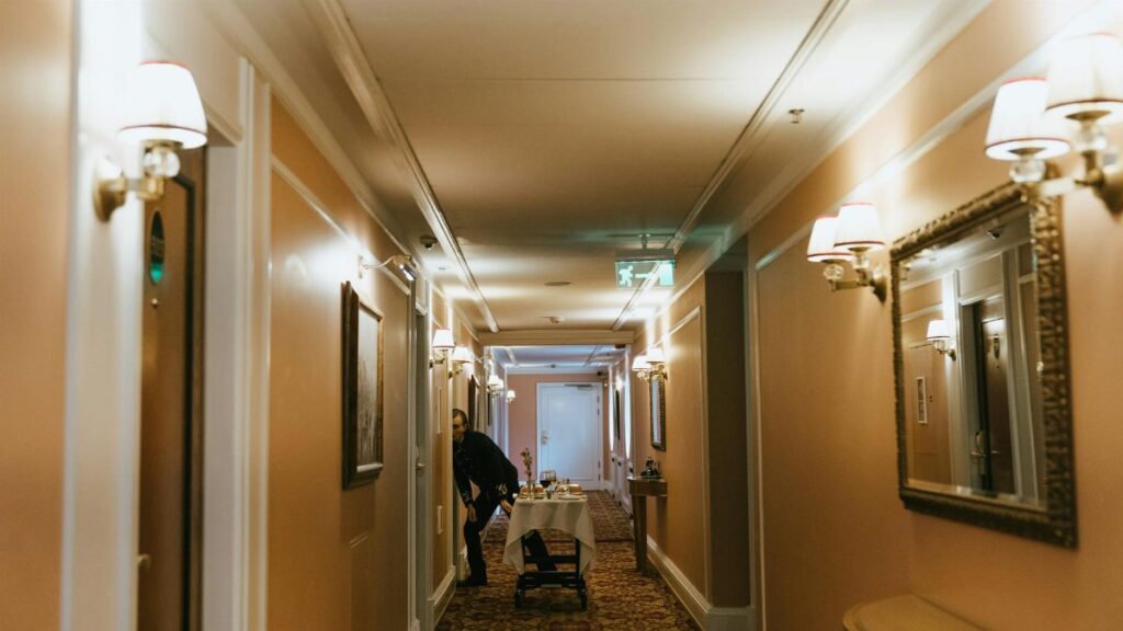 A hotel hallway with a staff member and room service trolley near guest rooms.