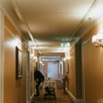 A hotel hallway with a staff member and room service trolley near guest rooms.