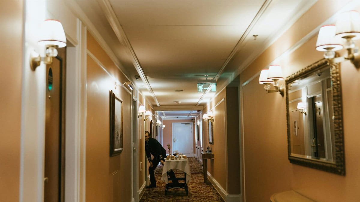 A hotel hallway with a staff member and room service trolley near guest rooms.