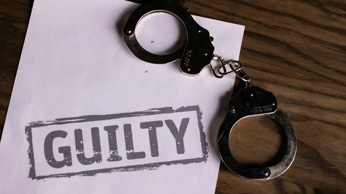Top view of handcuffs on paper with 'GUILTY' text, symbolizing a verdict or crime.