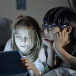 Two children using a tablet in a cozy home setting, engaging in screen time.
