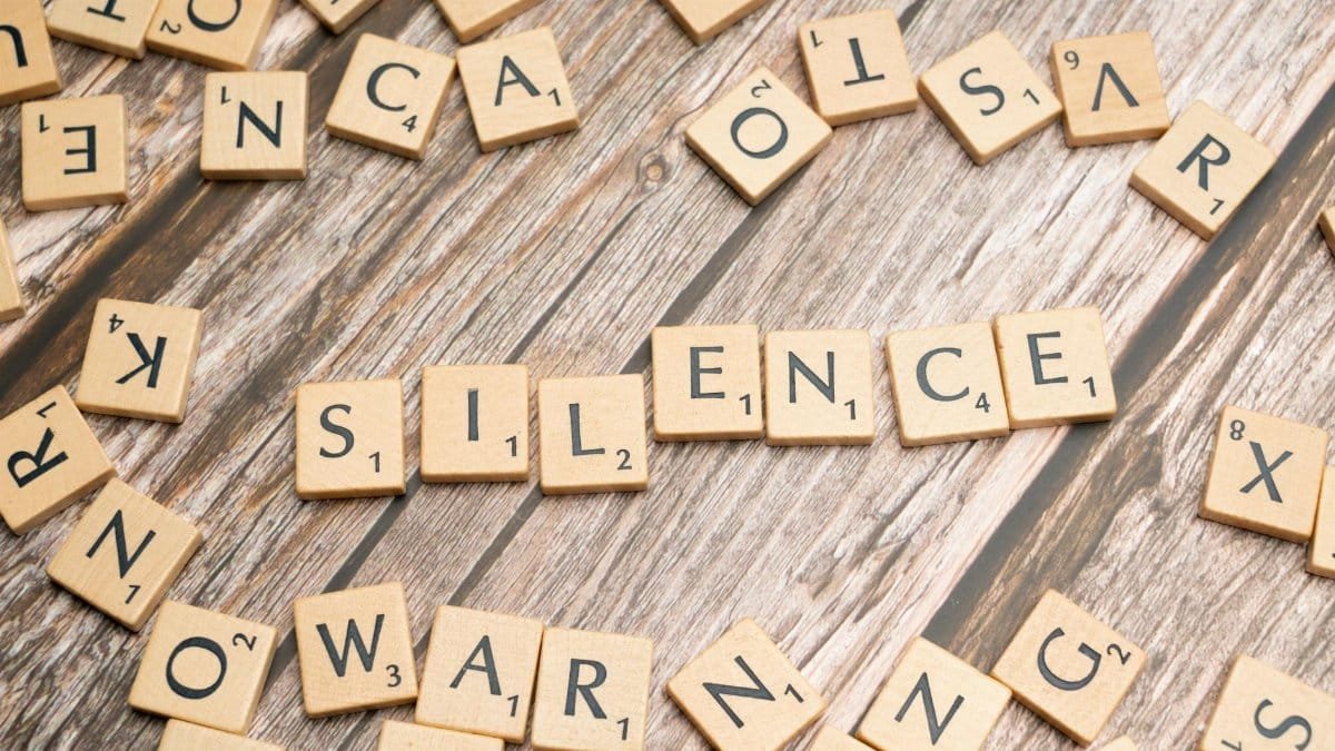 Wooden letter tiles arranged to spell 'silence' on a rustic wooden surface.