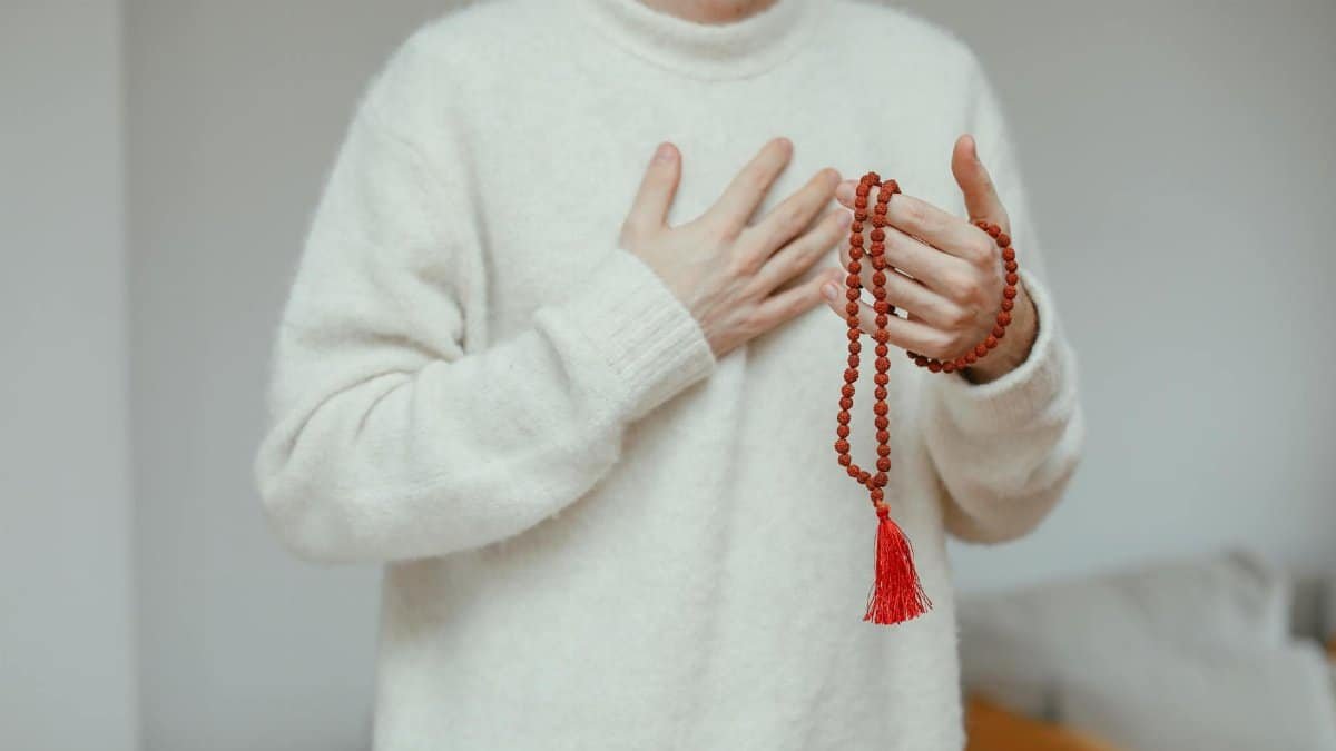 Close-up of person in a white knitted sweater holding red prayer beads, exuding calm and spirituality.