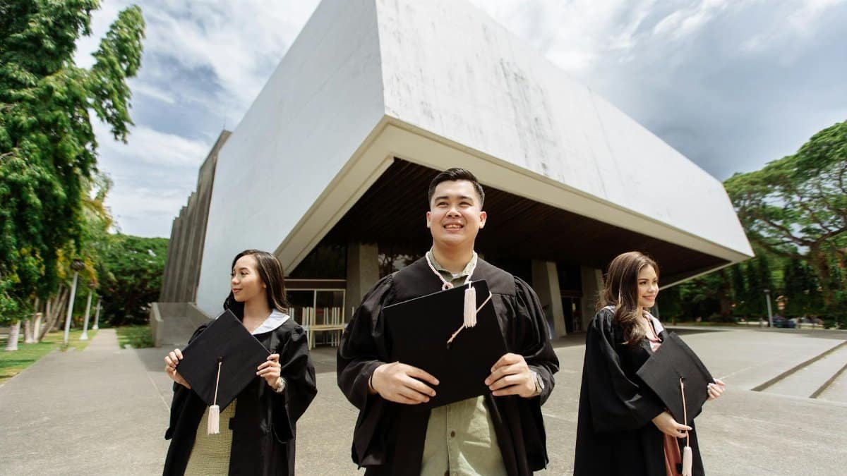 Three graduates celebrating outside a contemporary building with diplomas in hand.
