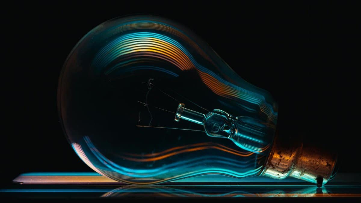 Creative close-up of a light bulb with colorful reflections against a black backdrop, symbolizing ideas and innovation.