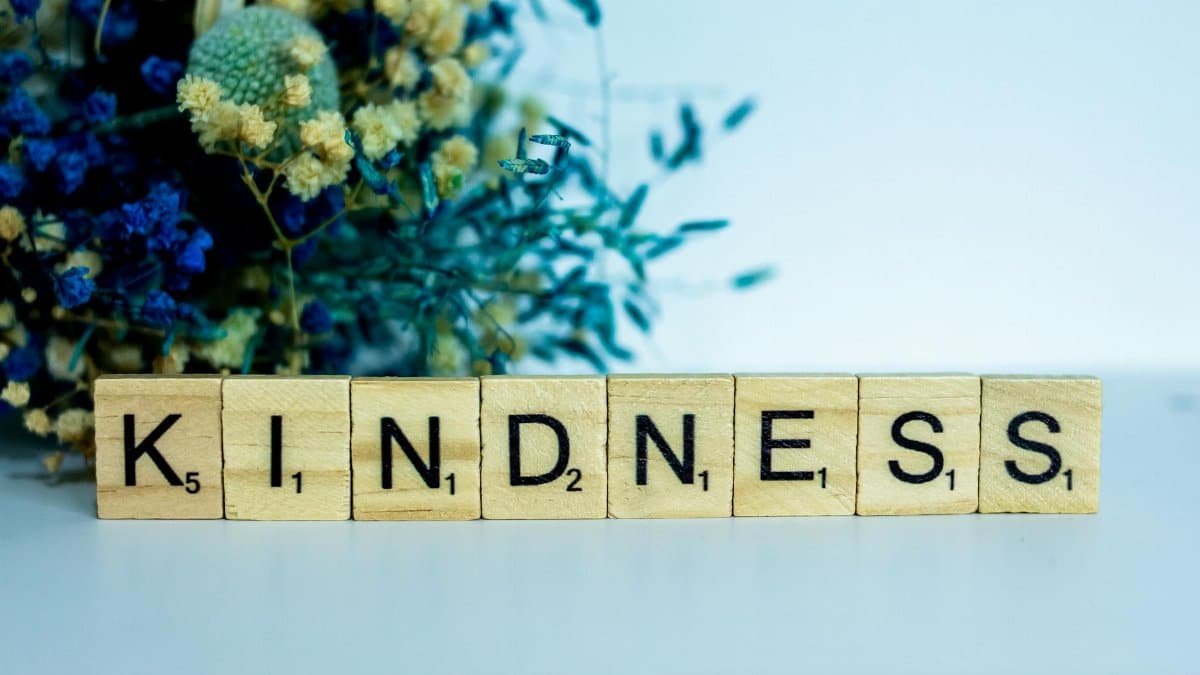 Scrabble tiles spelling 'KINDNESS' with colorful flowers in the background.