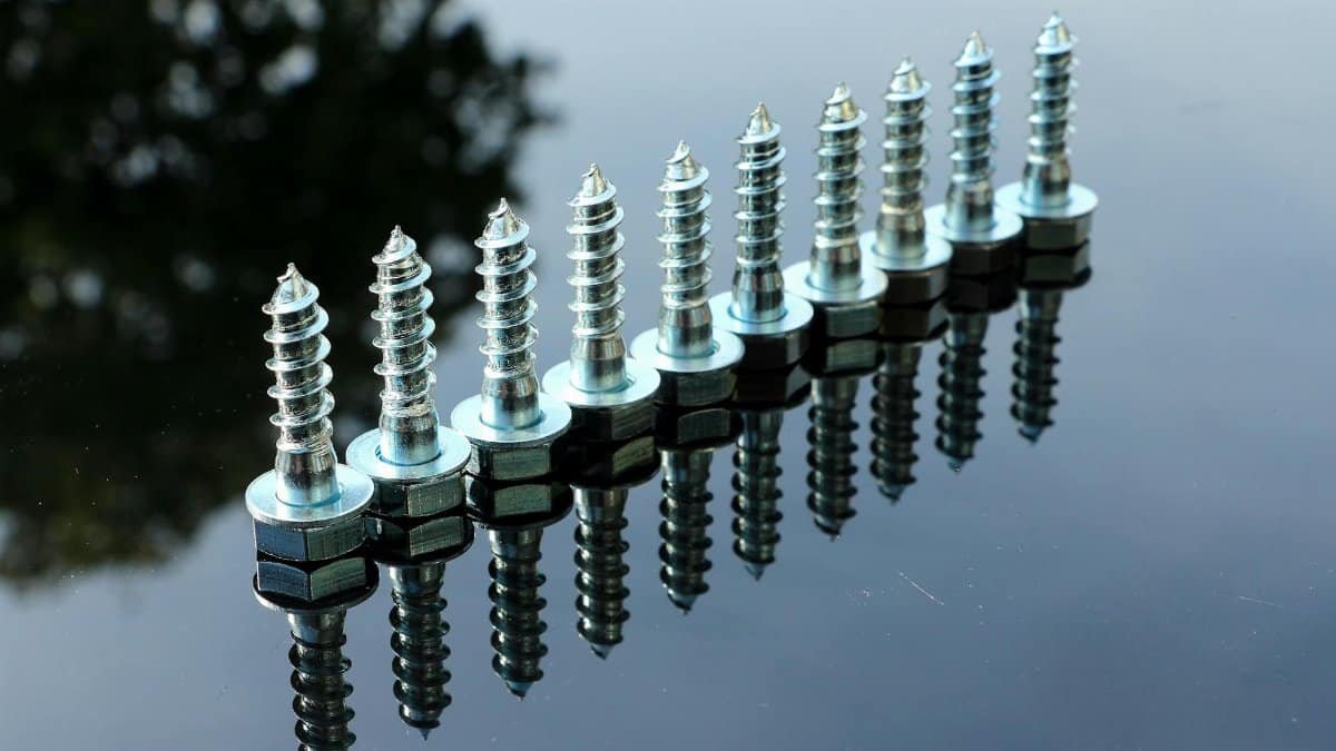A row of shiny metal screws on a reflective surface with clear reflections.