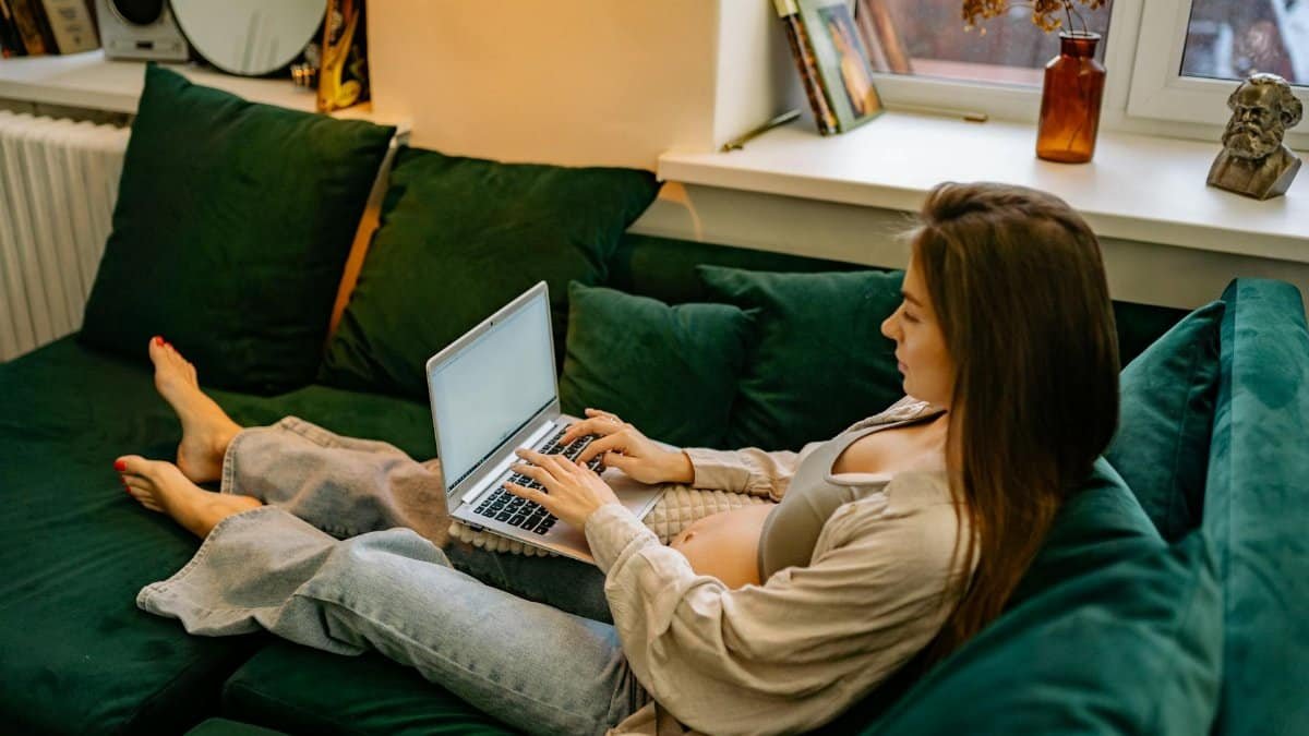 Expectant mother comfortably working from home on a laptop, showcasing modern maternity lifestyle.