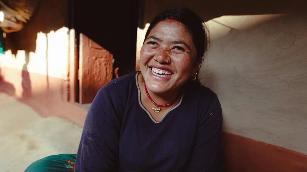 Smiling woman in traditional attire seated indoors, basking in natural light, exuding joy and warmth.