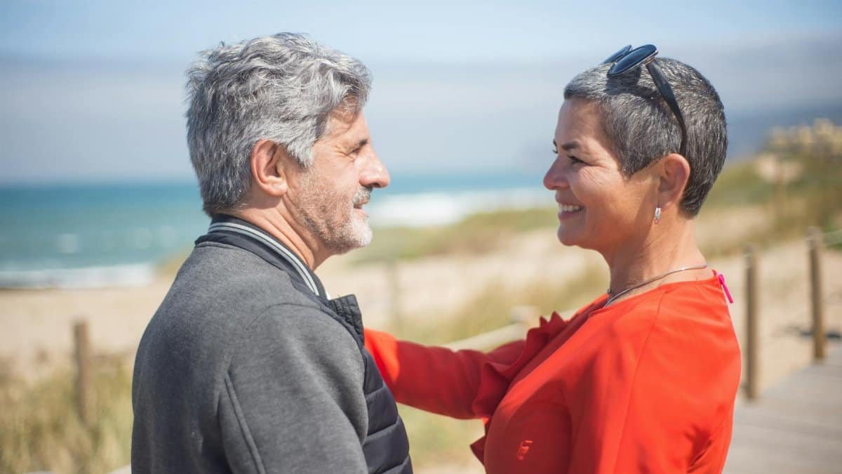 Mature couple smiling lovingly at each other on a sunny beach in Portugal.