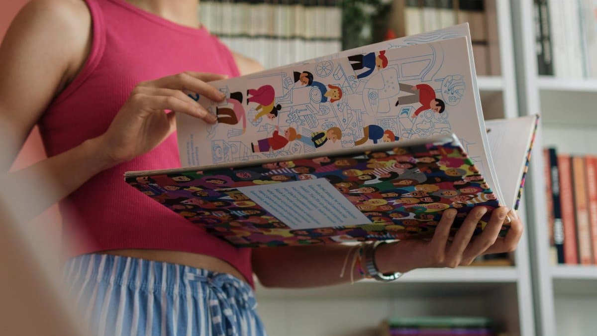 A person in colorful attire reads an illustrated book in a cozy library setting.
