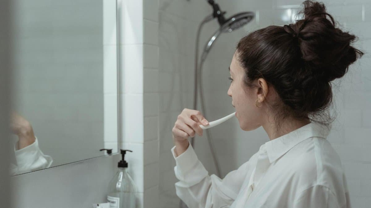 Woman brushing teeth in a modern bathroom, promoting daily oral health habits.