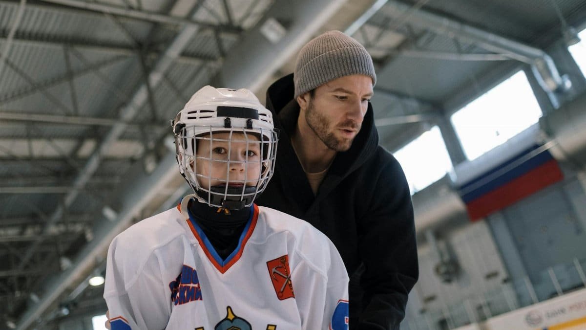A father teaching his son to play ice hockey inside an arena, focusing on learning and bonding.