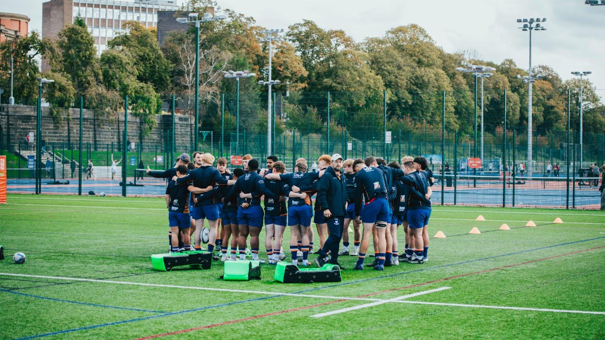 Team of rugby players huddling during outdoor training session on a sports field.