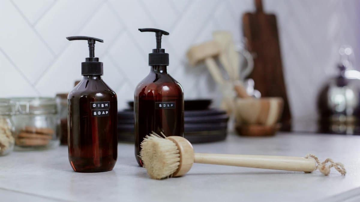 Aesthetic kitchen setting featuring amber soap bottles and dish brush for elegant cleaning.