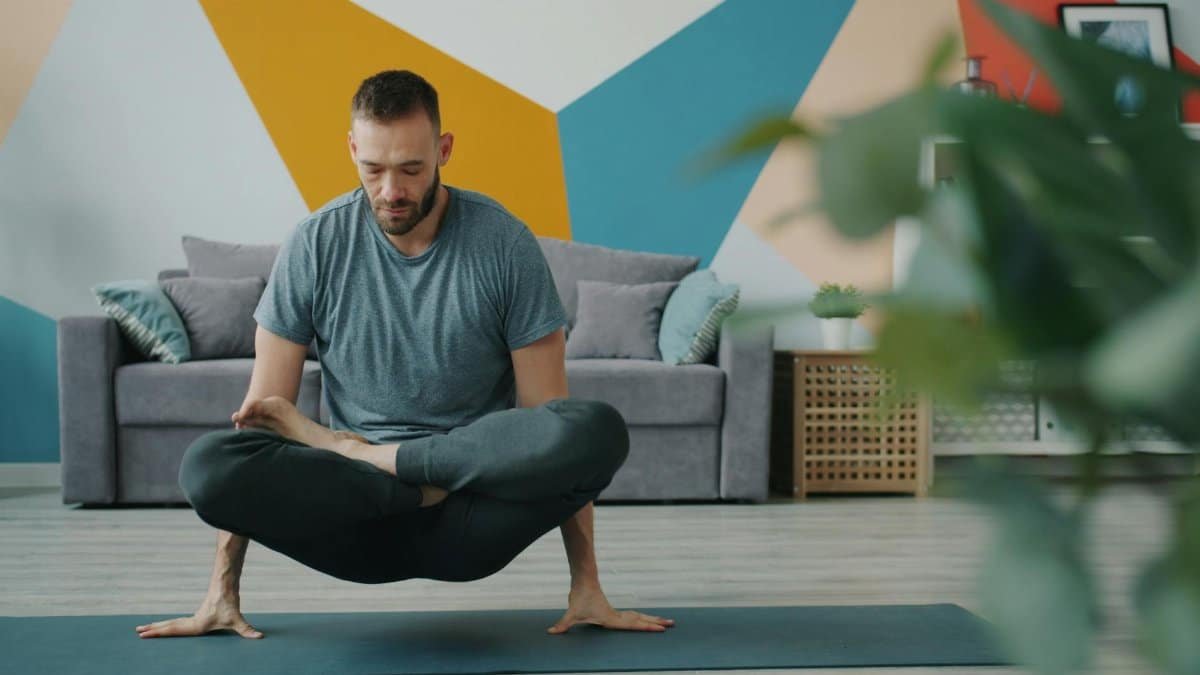 A man performing a challenging yoga posture in a modern living room with vibrant geometric wall art.