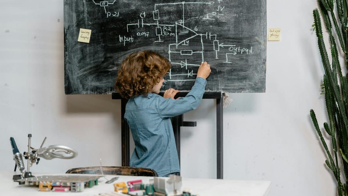 A young boy creatively draws a circuit diagram on a blackboard, showcasing intelligence and creativity.