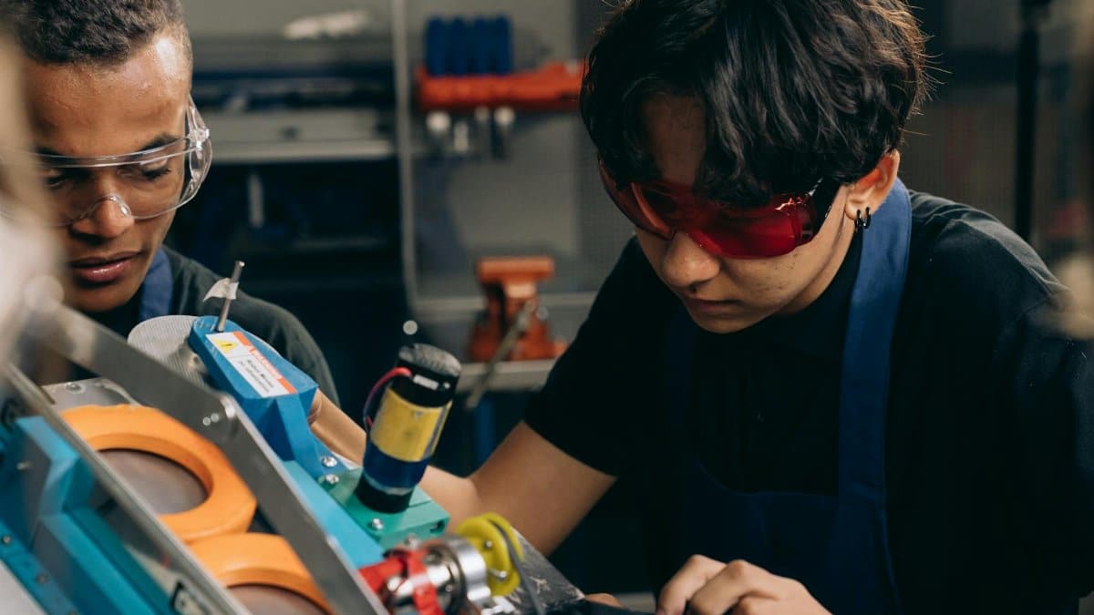 Two young engineers concentrating on precision work in a technical workshop, wearing safety goggles.