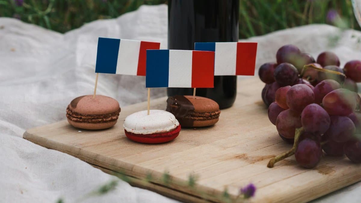 Macarons decorated with French flags on a picnic setup with grapes and wine.