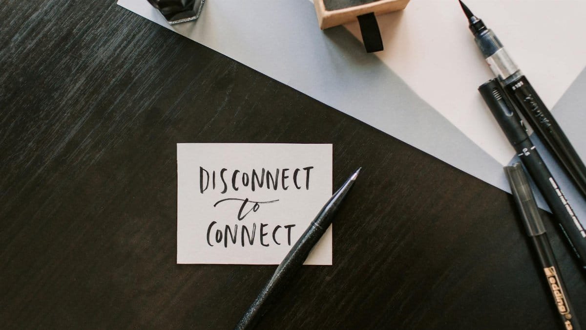 A flat lay image featuring a handwritten note with pens on a wooden surface, promoting mindful connection.