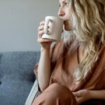 Woman with wavy blonde hair sipping coffee in casual indoor setting.
