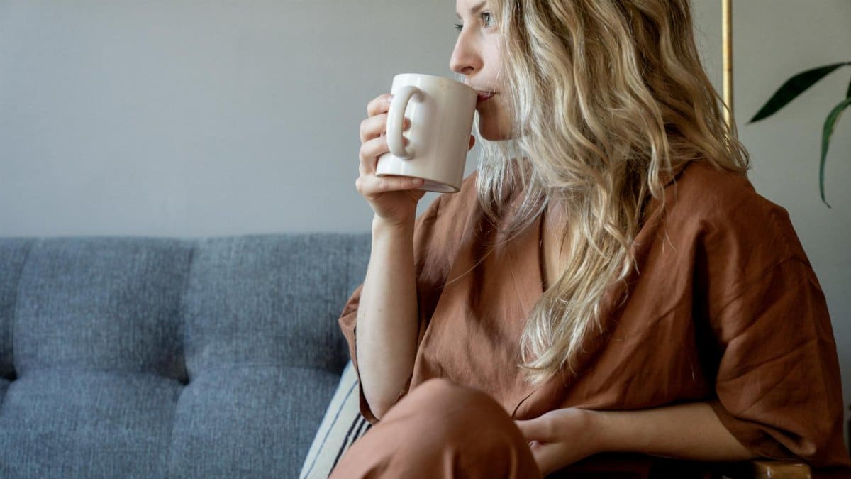 Woman with wavy blonde hair sipping coffee in casual indoor setting.