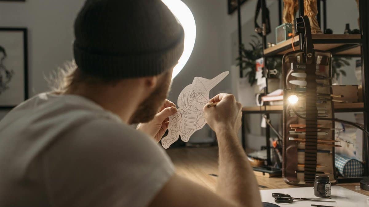 A tattoo artist focusing on a detailed drawing in a well-lit, artistic workspace.