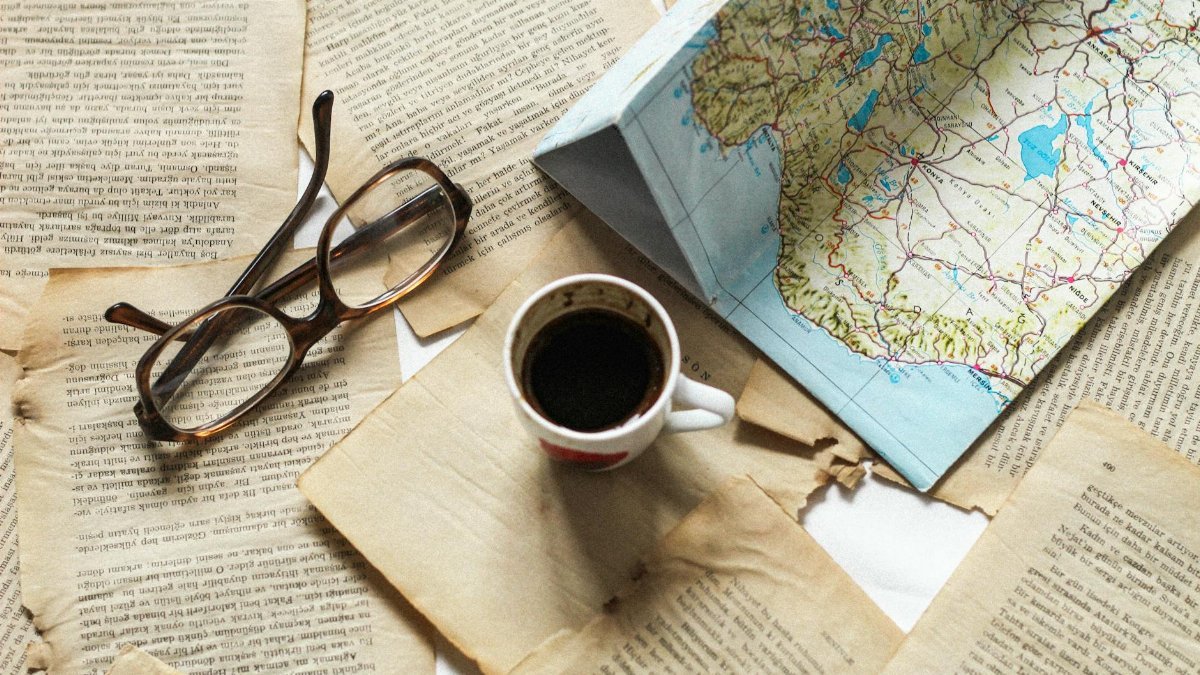 A flat lay of vintage papers, a coffee cup, a folded map, and eyeglasses creates a nostalgic travel theme.