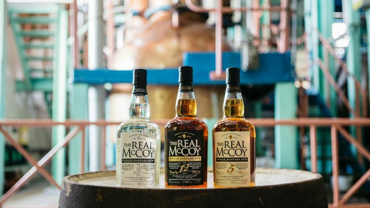 Three bottles of The Real McCoy rum displayed on a barrel inside a distillery.
