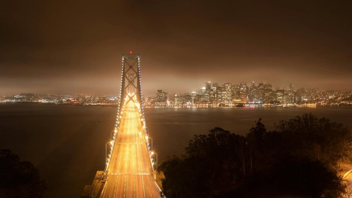 Aerial view of the Golden Gate Bridge leading to illuminated San Francisco skyline at night.