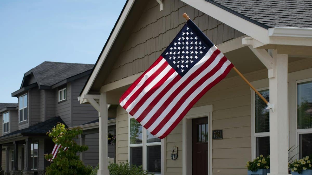 A vibrant American flag displayed outside a stylish suburban house in daylight.