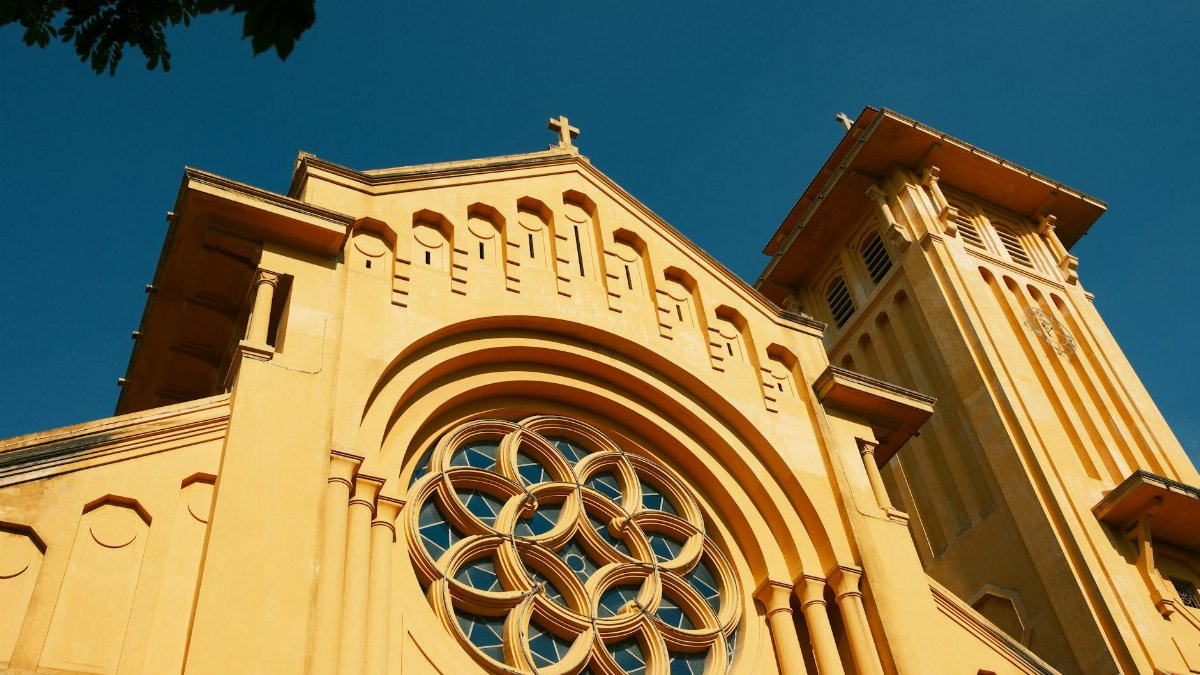 Striking image of a yellow Catholic church facade against blue sky in Hanoi, Vietnam.