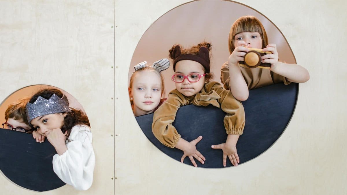 Group of children playing indoors, peeking through circular holes, showcasing imagination and diversity.