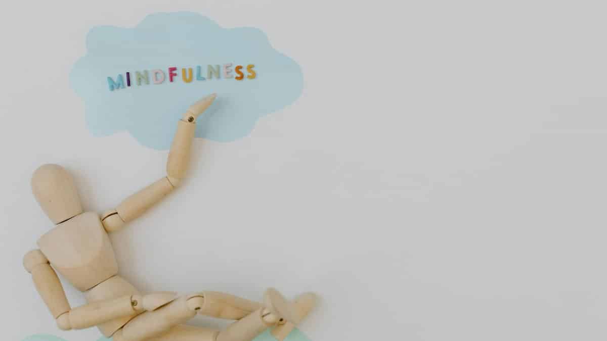 Wooden mannequin with mindfulness text on light blue cloud background, conveying calm.