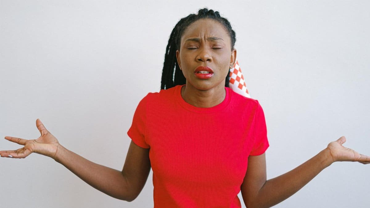 Portrait of a woman in a red shirt expressing confusion with her eyes closed and arms out. Ideal for emotion concepts.