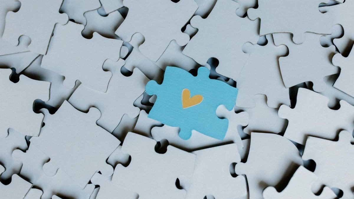 A standout blue puzzle piece with a heart symbol among white puzzle pieces, showing uniqueness.