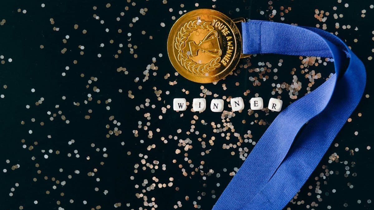 A gold medal with a blue ribbon on a black surface with glitter, symbolizing success.