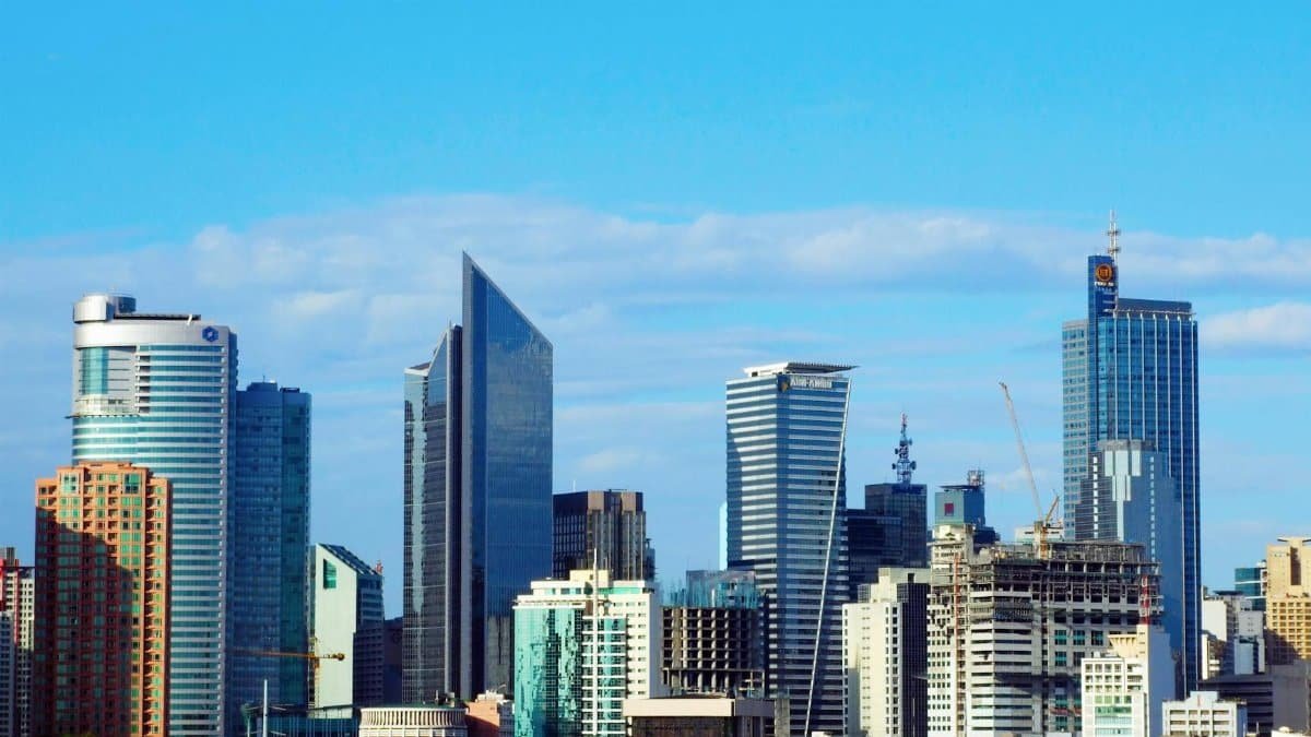 Bright daytime view of Makati City's modern skyline featuring prominent skyscrapers under a clear blue sky.