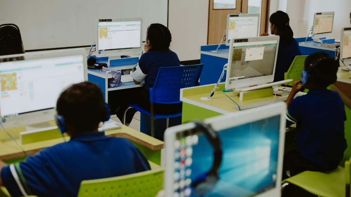 Children engaged in learning at computers in a modern classroom setting, promoting digital literacy.