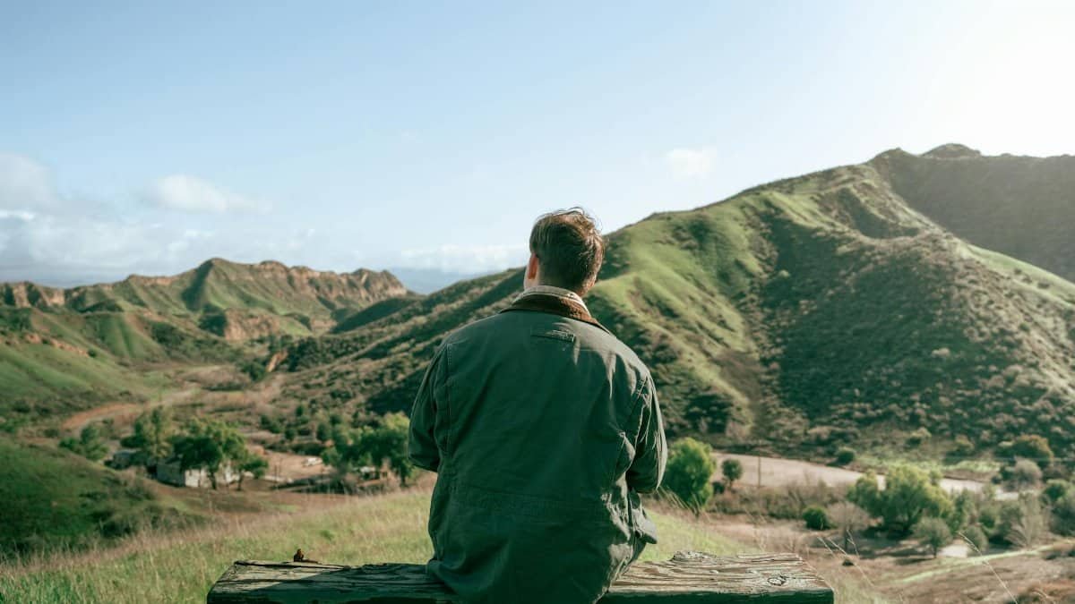 Man sitting on a bench overlooking a scenic mountain landscape.