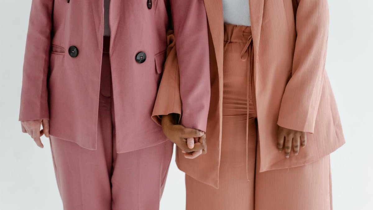 Two women in chic suits holding hands, symbolizing support and solidarity.